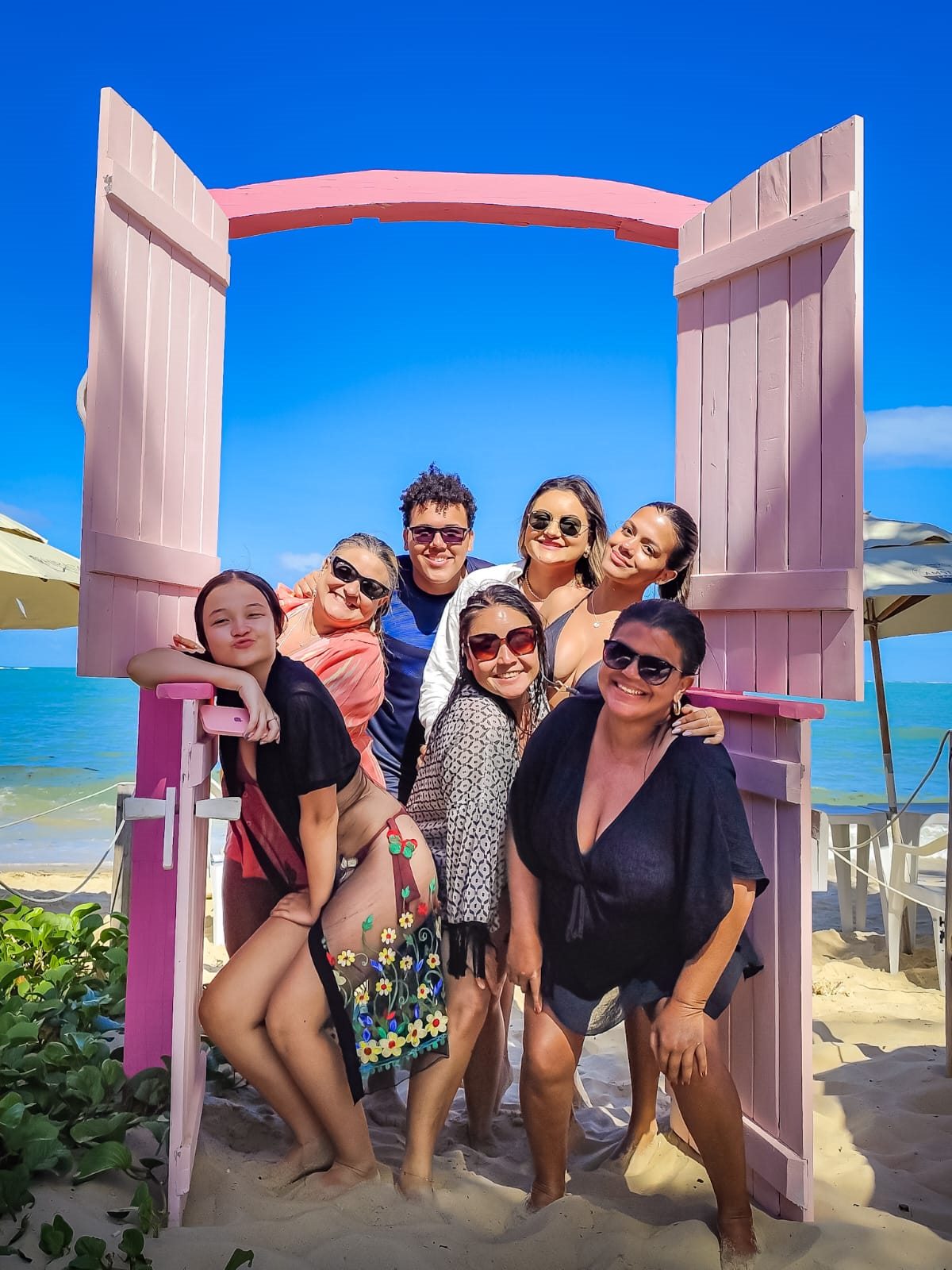 Grupo de visitantes reunido na porta rosa do Hibisco Praia diante do mar