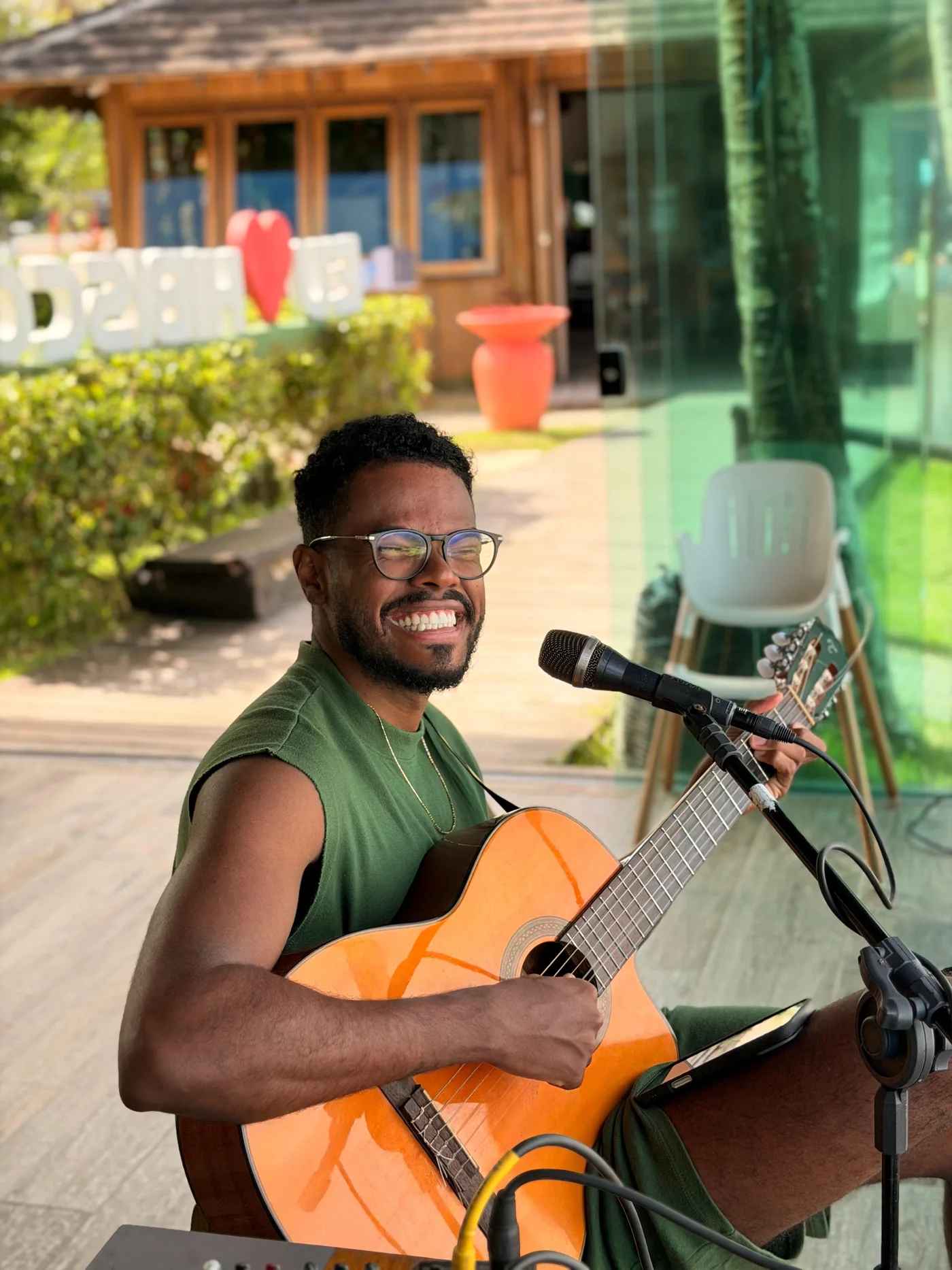 Músico sorrindo enquanto canta e toca violão no Hibisco Praia